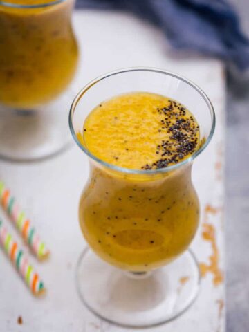 Two glasses of golden milk smoothie topped with poppy seeds