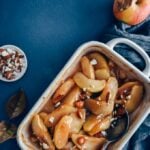 Cinnamon baked apple slices in a baking pan accompanied by apples and almonds.