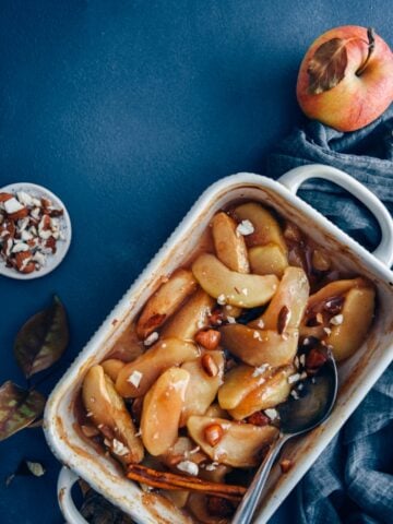 Cinnamon baked apple slices in a baking pan accompanied by apples and almonds.