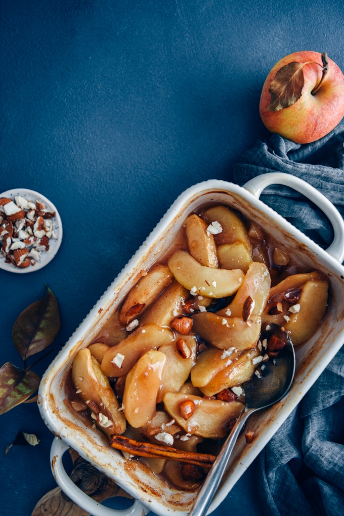 Cinnamon baked apple slices in a baking pan accompanied by apples and almonds.