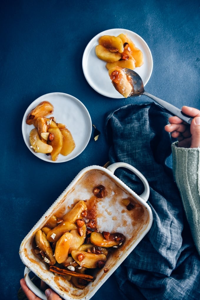 These cinnamon baked apple slices are like the gluten-free and vegan version of apple pie. Way easier to make! A perfect light dessert for fall. #applerecipe #falldessert #bakedappleslices Hands serving baked apple slices on white plates