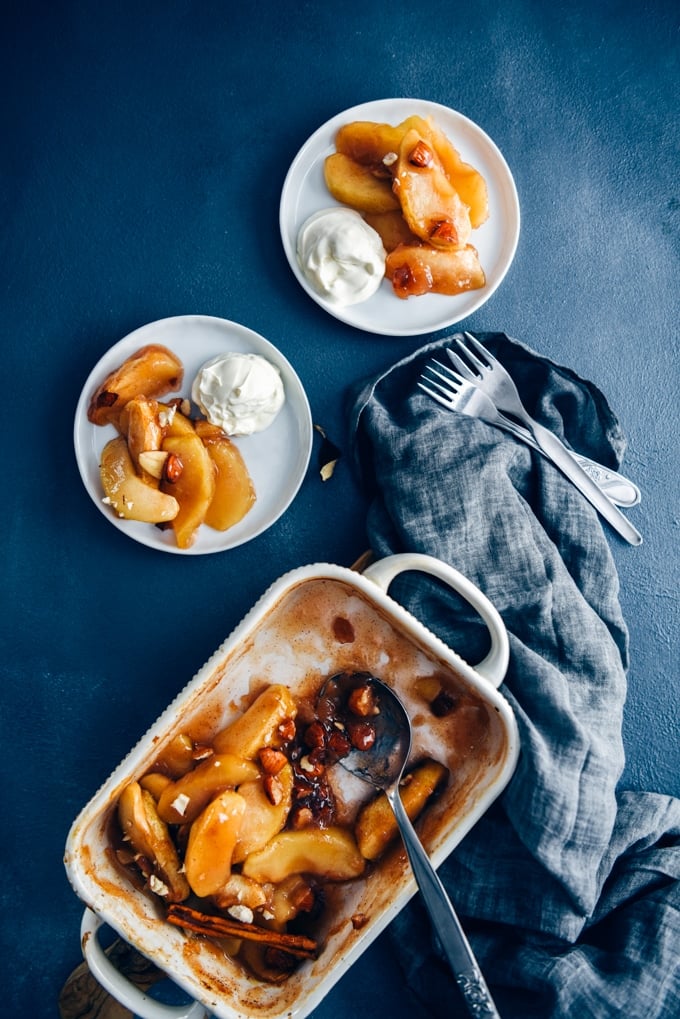 Cinnamon baked apple slices in a baking pan accompanied by two white plates with baked apple slices.