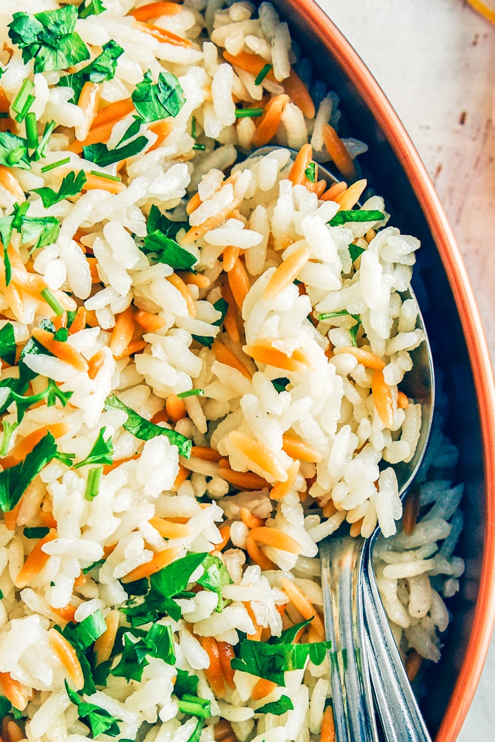 Fluffy rice pilaf with orzo in a copper pan with two spoons in it.