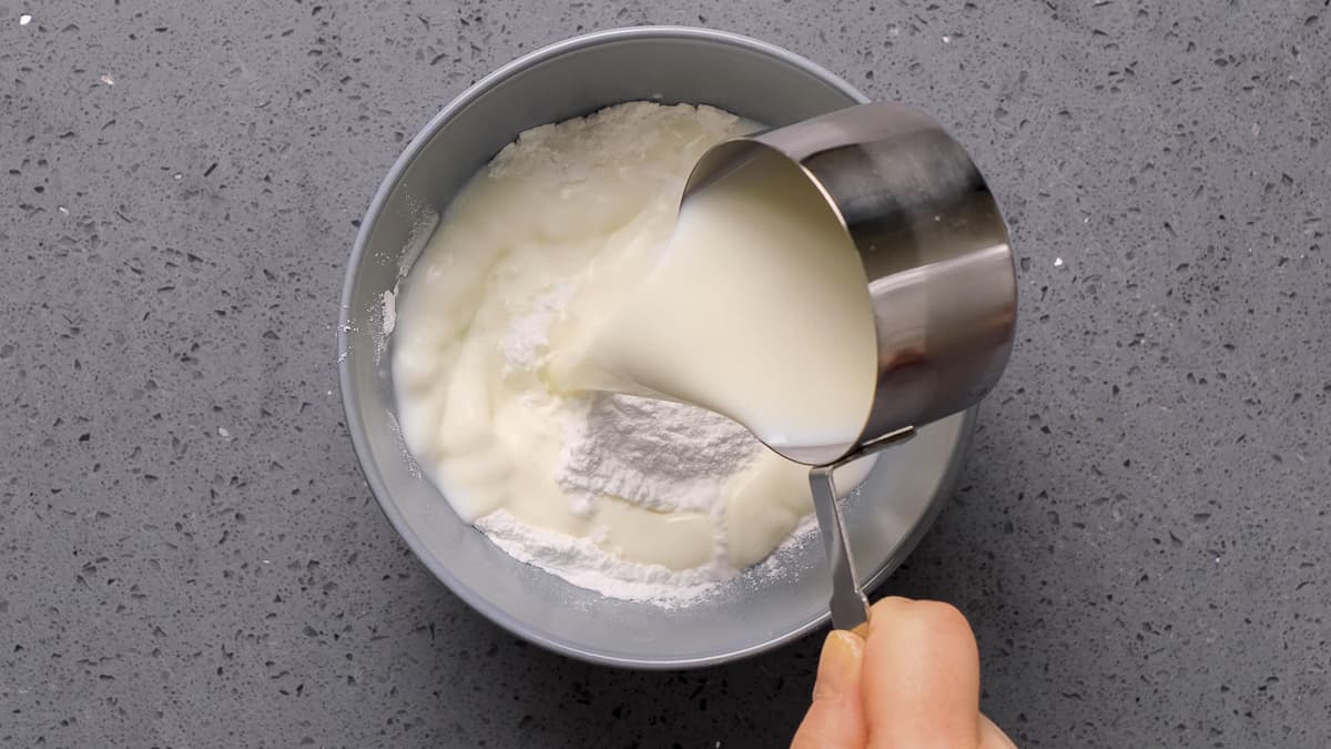 Hand pouring milk over corn strach in a bowl.