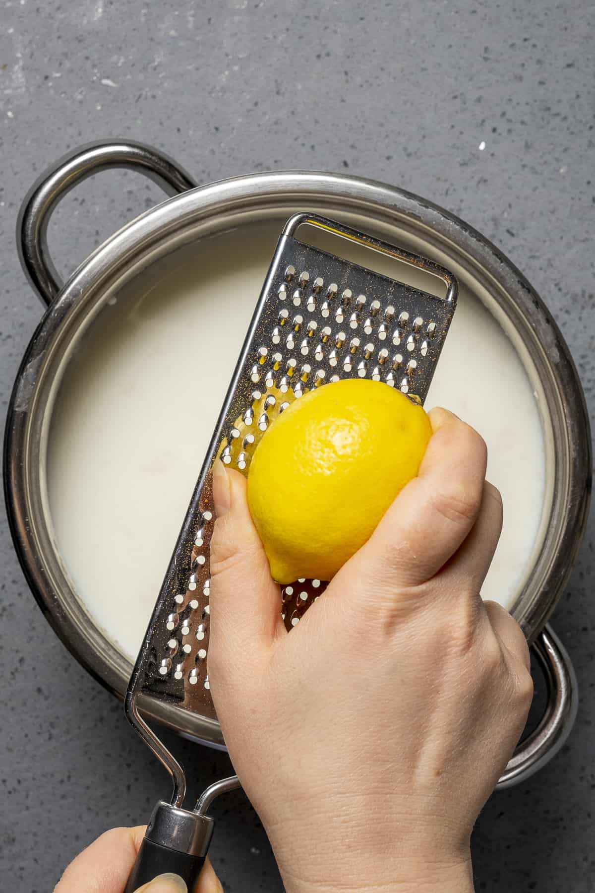 Hands grating lemon zest into simmering milk.