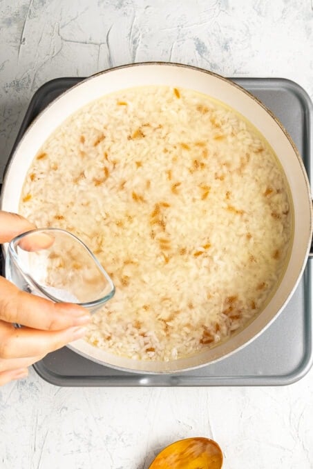 A hand pouring water over rice in a white pan over the stove.