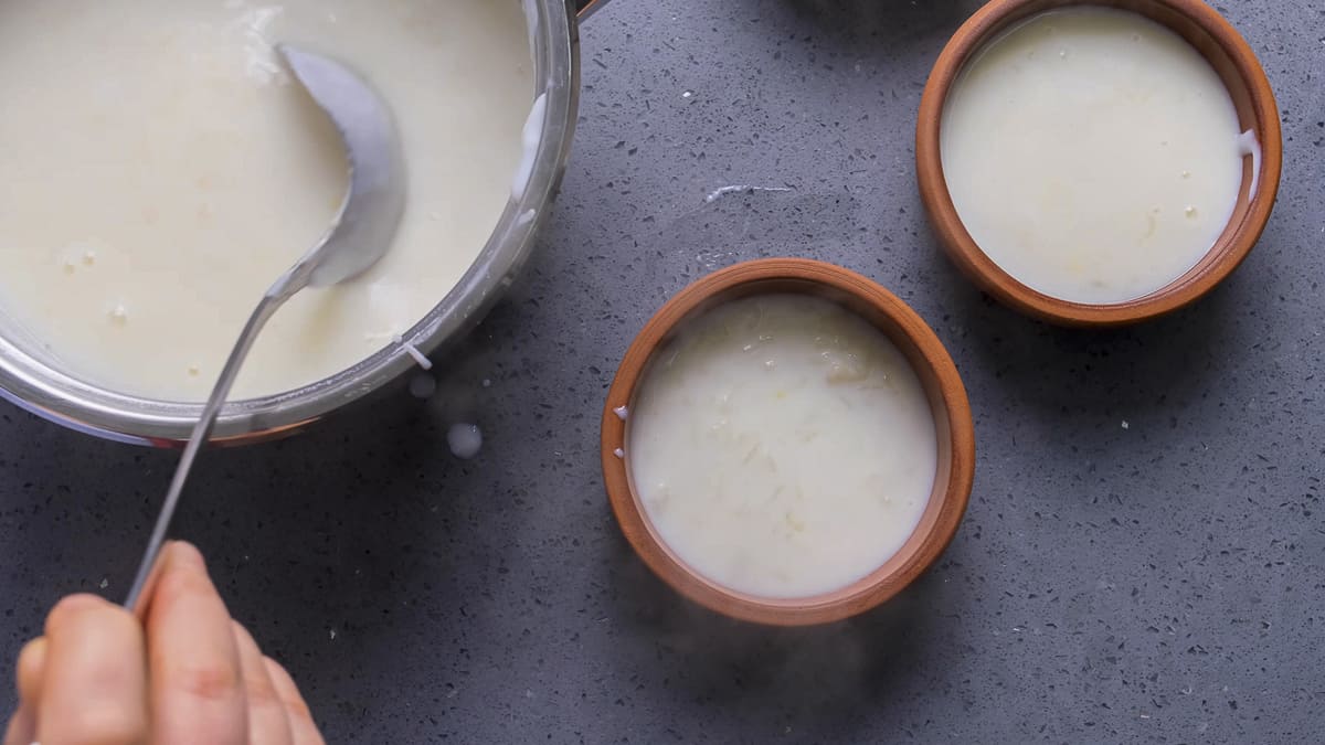 Hands sharing cooked rice pudding into small bowls.