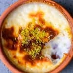 Baked sütlaç with caramelized top and pistachio topping in a clay bowl.