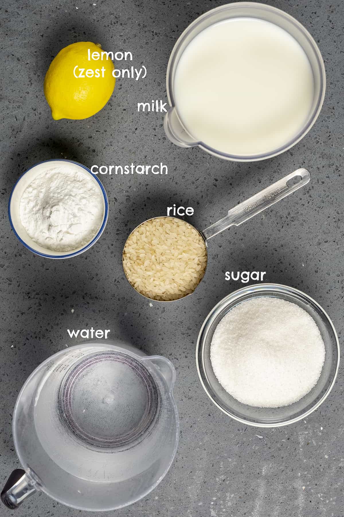 Milk, rice, lemon, cornstarch, water, sugar on a grey background.