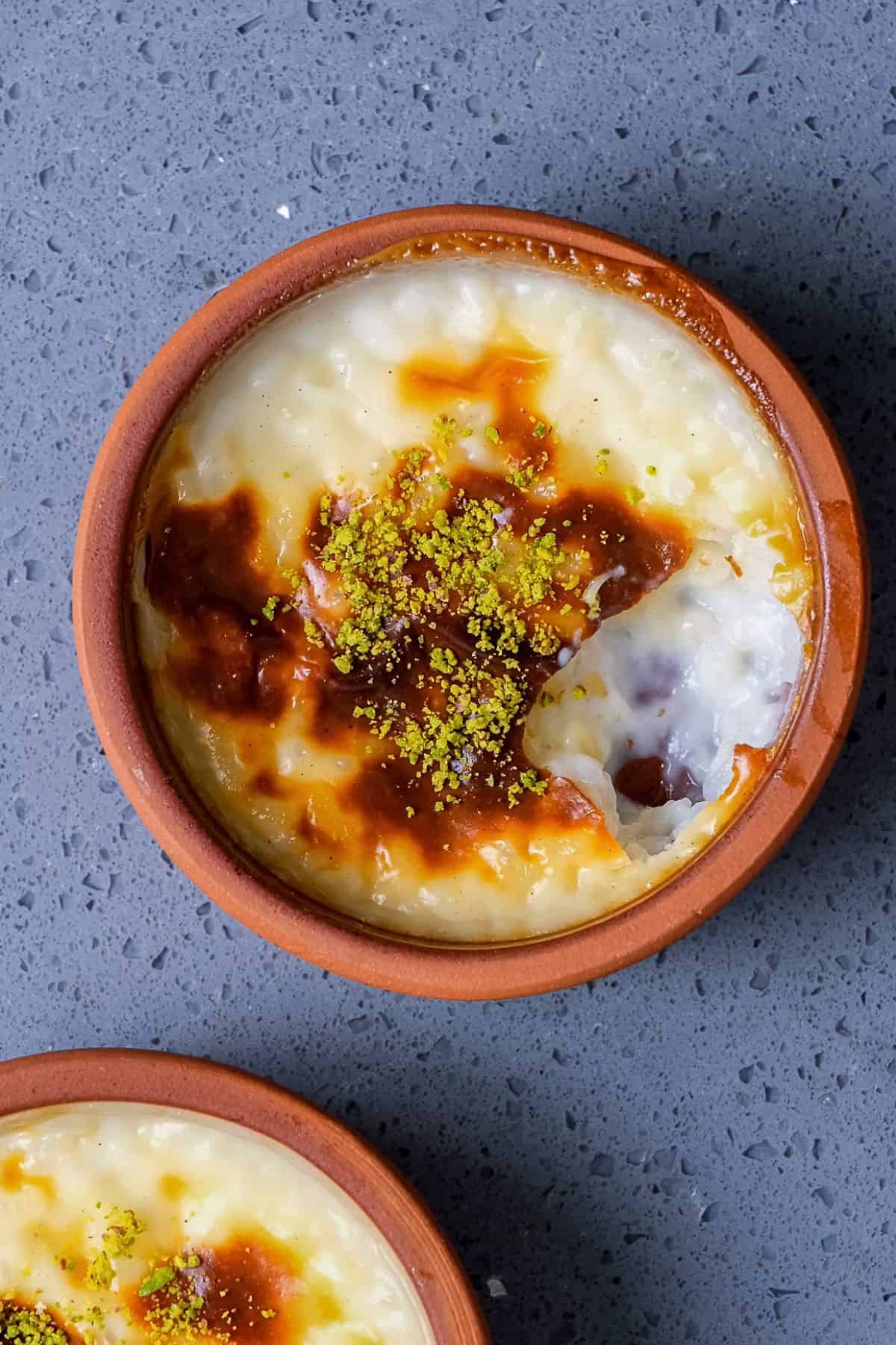 Top view of Turkish baked rice pudding (fırın sütlaç) in clay bowls with caramelized tops and ground pistachios.