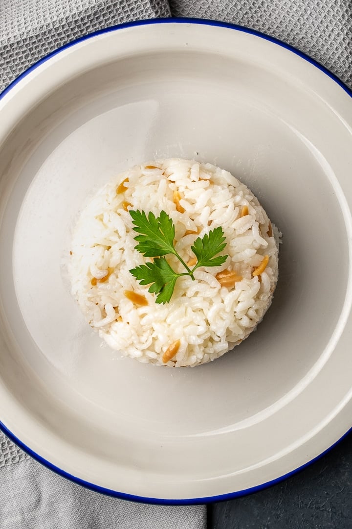 Turkish style rice pilav served in the shape of a dome with a sprig of parsley on the top on a white plate.