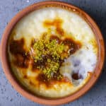 Rice pudding with a golden top garnished with pistachios in a clay bowl.