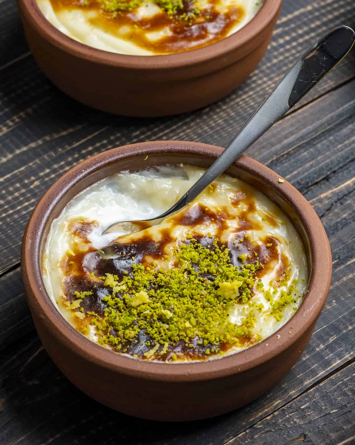 Sutlac garnished with pistachios in a clay bowl and a spoon in it.