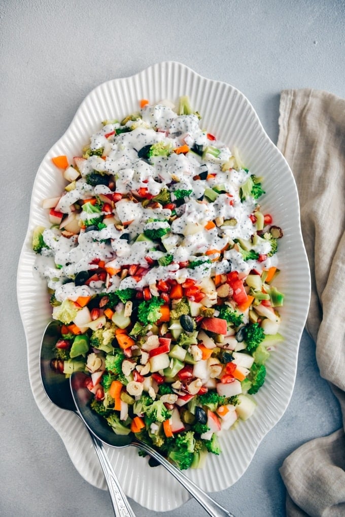 Broccoli apple salad with carrots, nuts and pumpkin seeds drizzled with poppy seed yogurt dressing photographed in a white oval bowl from top view.