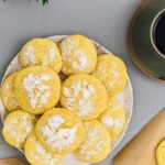 Lemon crinkle cookies on a white plate with a cup of coffee on the side.