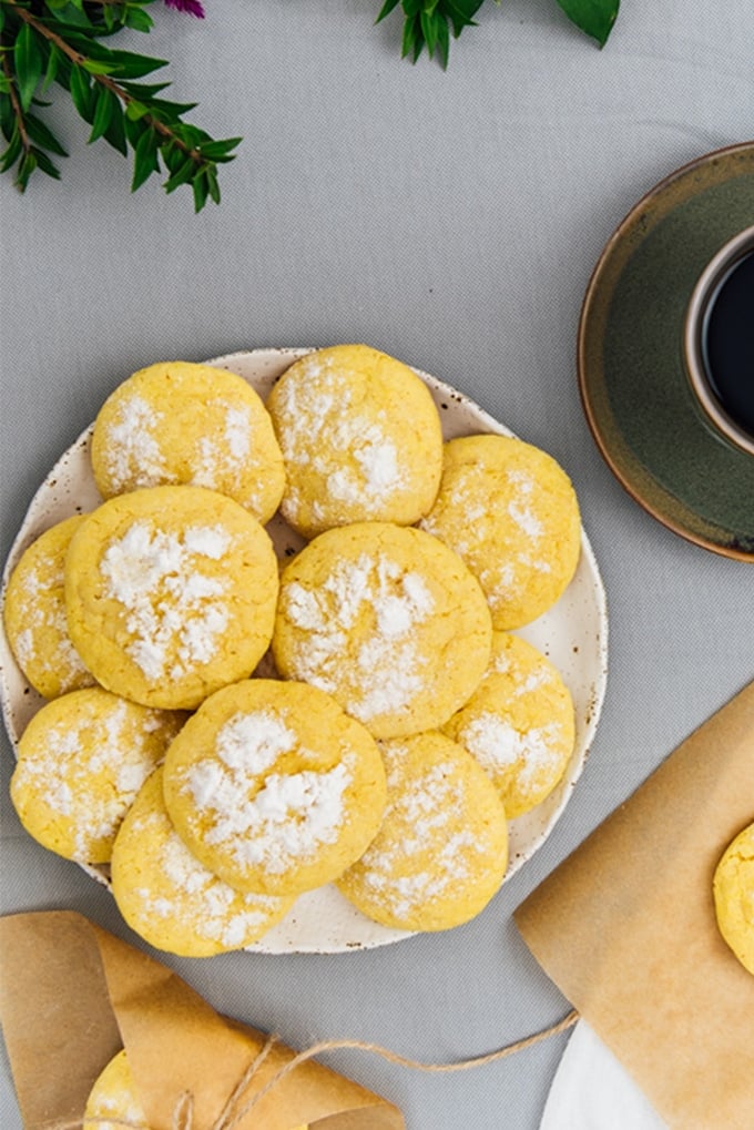Lemon crinkle cookies on a white plate with a cup of coffee on the side.