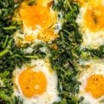 Eggs cooked with sautéed spinach in a skillet for a simple spinach and eggs breakfast.