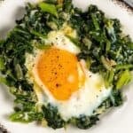 Egg cooked with sautéed spinach served on a white plate.