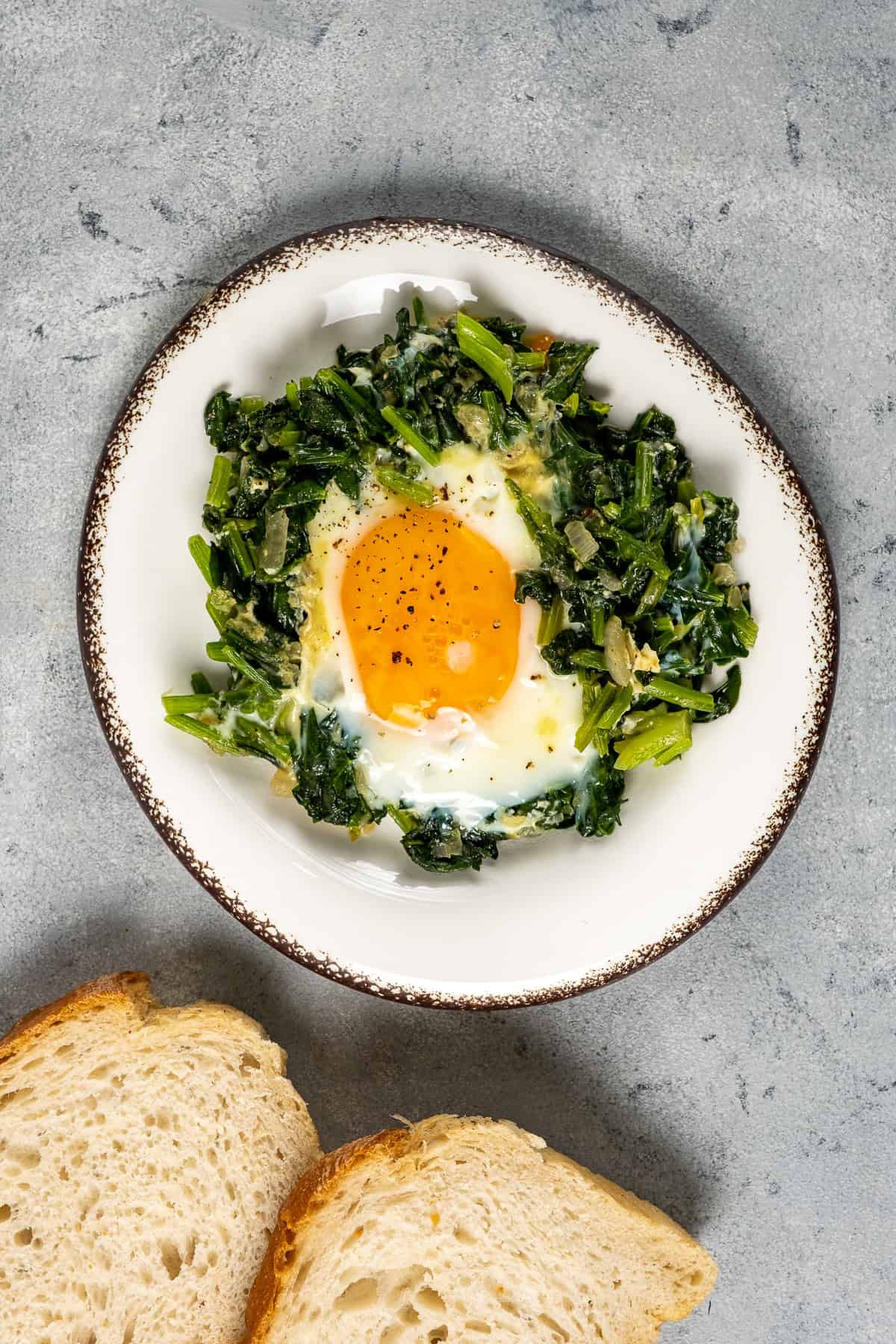 A plate of sautéed spinach topped with a sunny-side-up egg, served with slices of bread on the side.