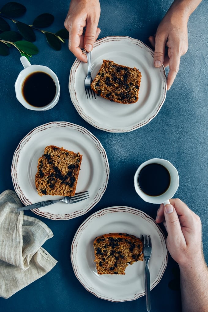 Two people having breakfast with chocolate chip banana bread served on white plates and tea.