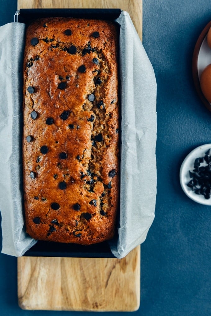 Chocolate chip banana bread in a baking pan on a wooden cutting board.