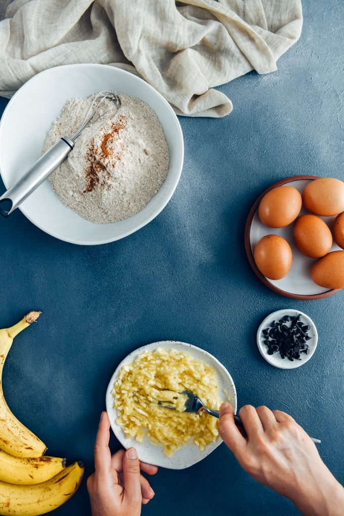 Hands mashing bananas to make chocolate chip banana bread.