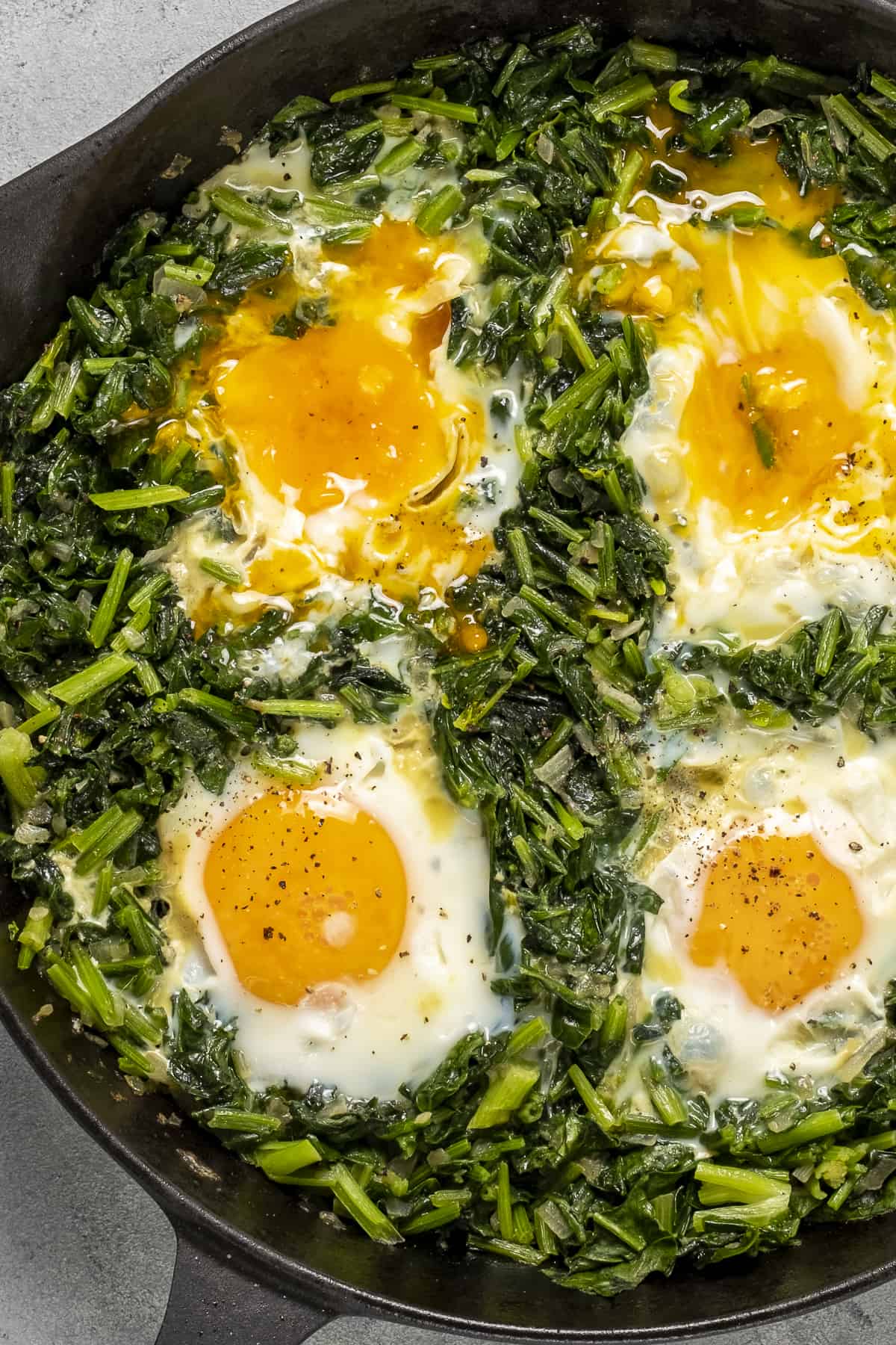Spinach and 4 whole eggs cooked in a pan.