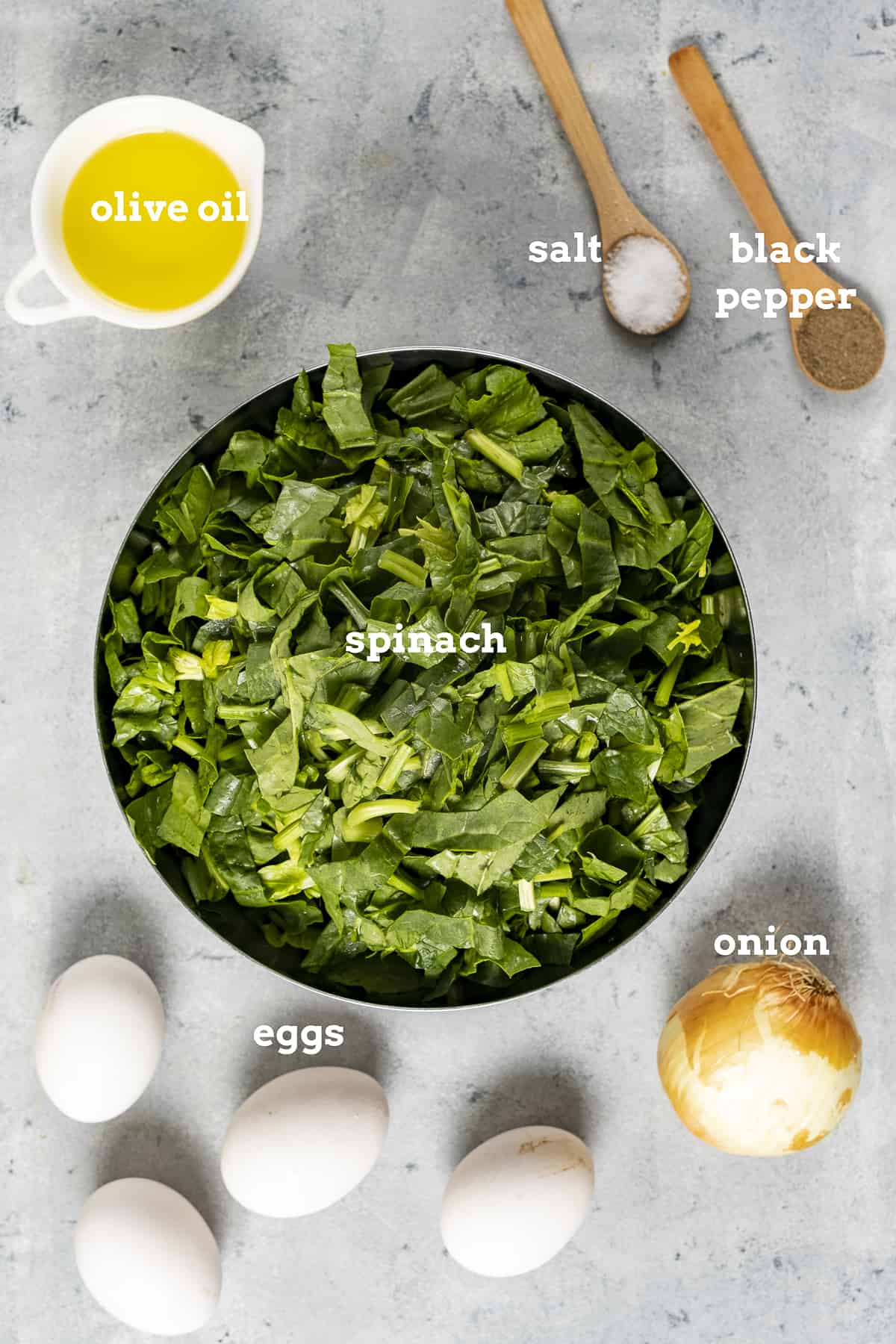 Chopped spinach, olive oil, salt and pepper, eggs and onion on a grey background.