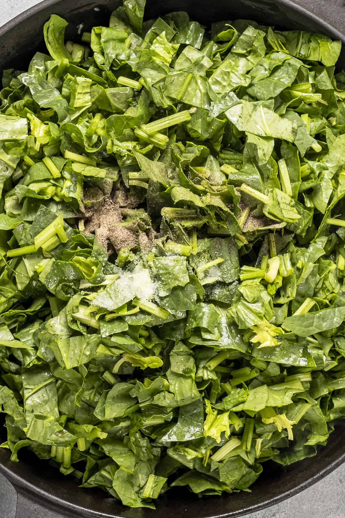 Chopped spinach, salt and pepper in a pan.