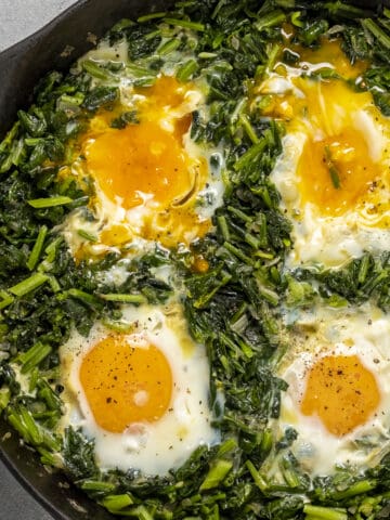 Spinach with runny yolk eggs in a pan.