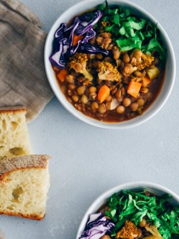 Vegan lentil stew with broccoli and carrot garnished with shredded red cabbage and chopped parsley served in white bowls.