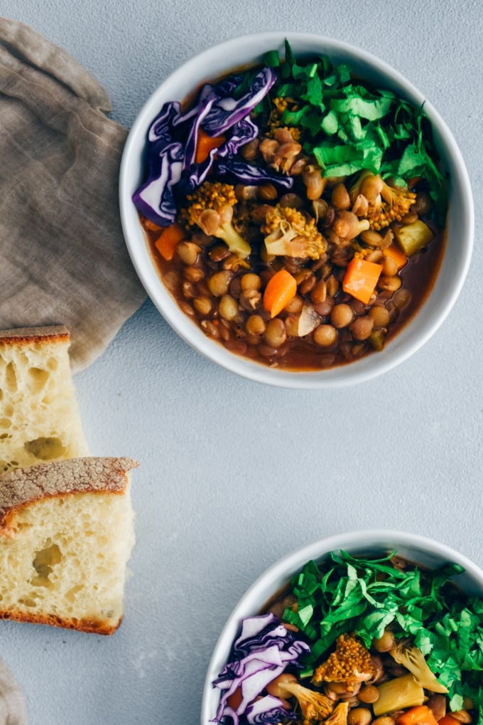 Vegan lentil stew with broccoli and carrot garnished with shredded red cabbage and chopped parsley served in white bowls. 