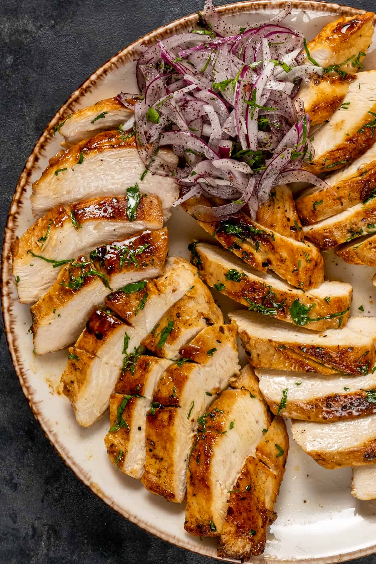 Cast iron pan cooked chicken breasts sliced and served with sumac onions on a plate.