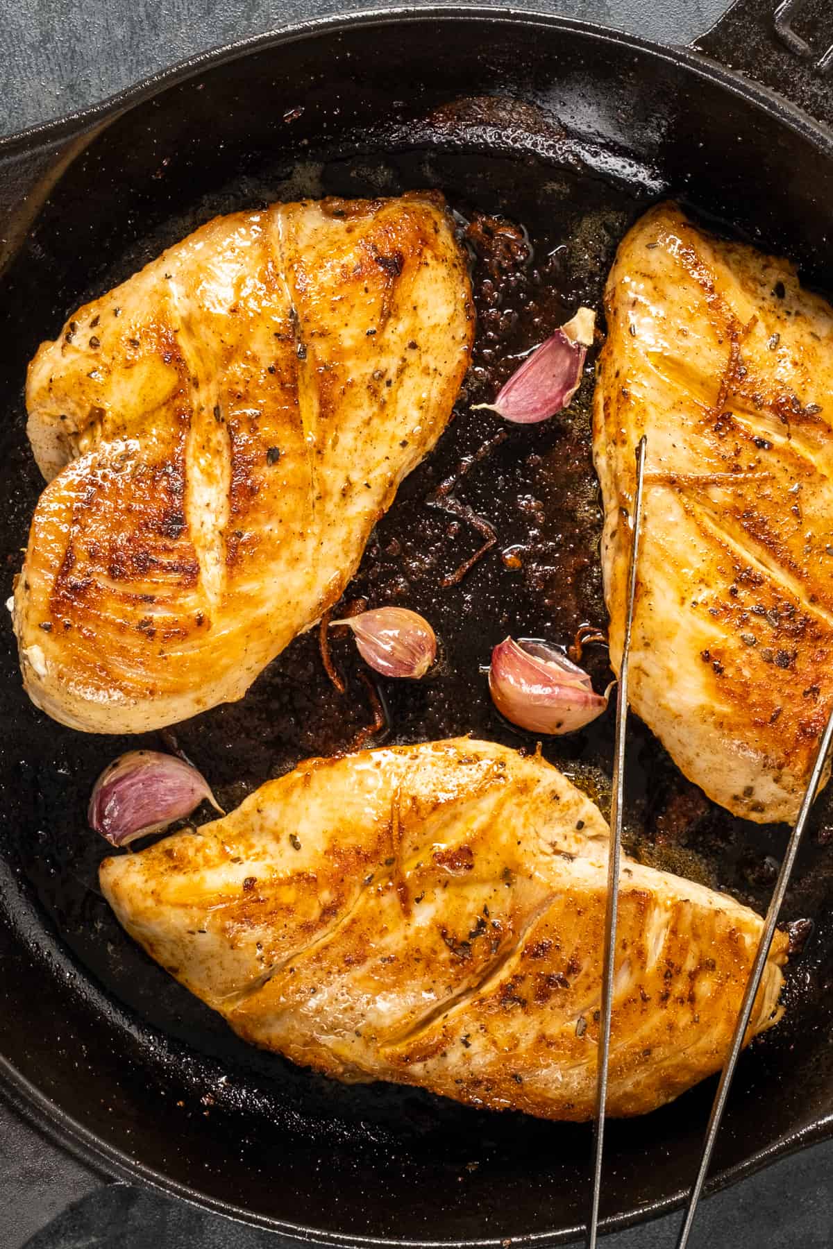 Golden cooked chicken breasts and garlic cloves with their skin in a cast iron pan.