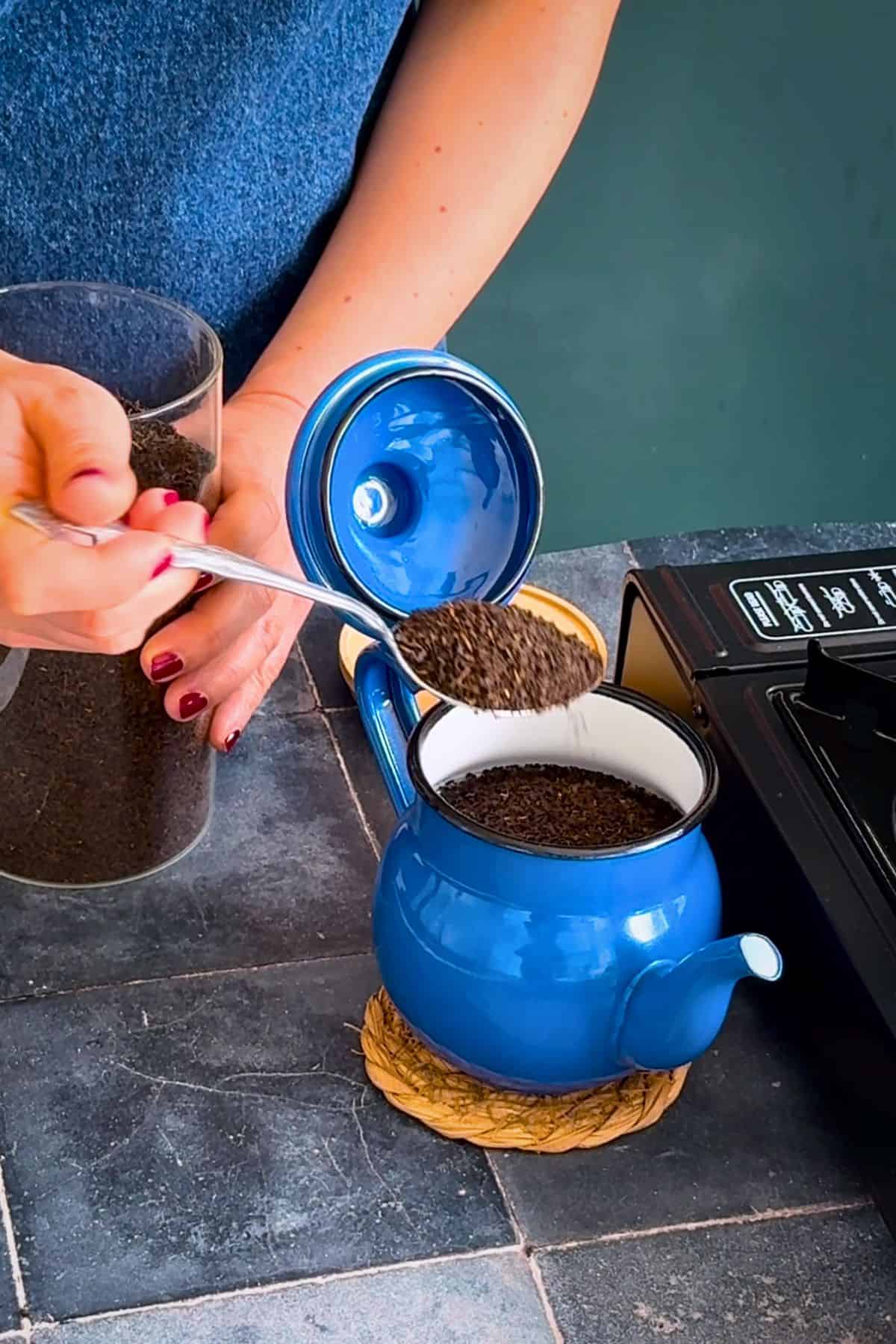 Loose black tea leaves being added to the upper pot of a blue Turkish double teapot (çaydanlık).