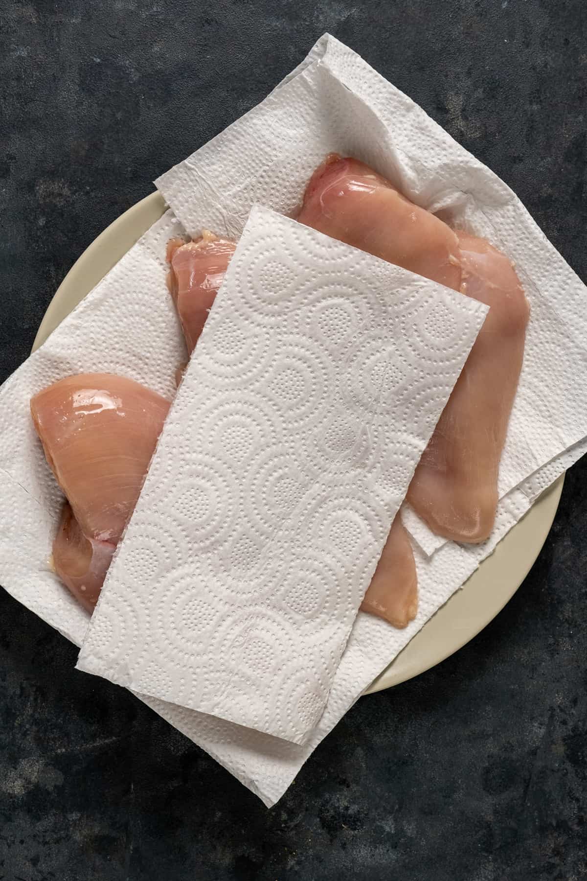 Chicken breasts on a plate lined with paper towel and another piece of paper towel on them.