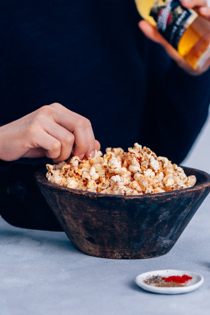 Woman eating spicy popcorn in a wooden bowl for easy game day snacks