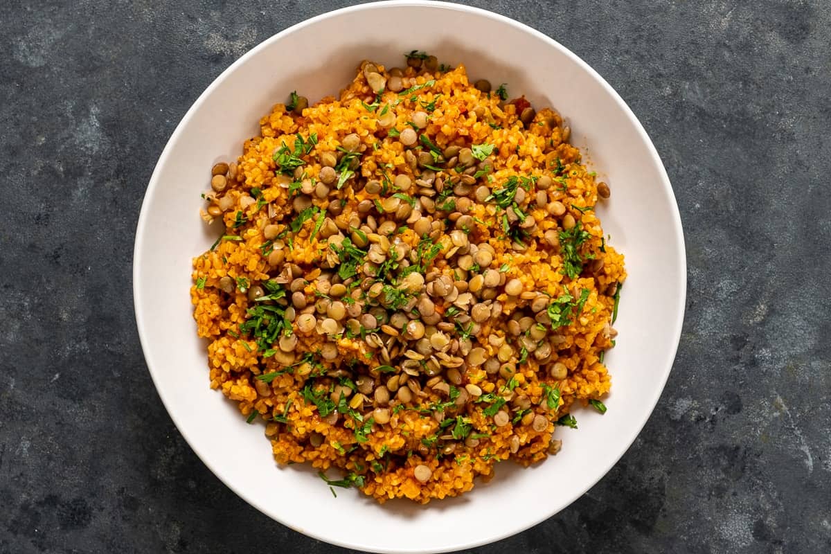 Bulgur pilaf topped with green lentils and parsley in a white bowl.