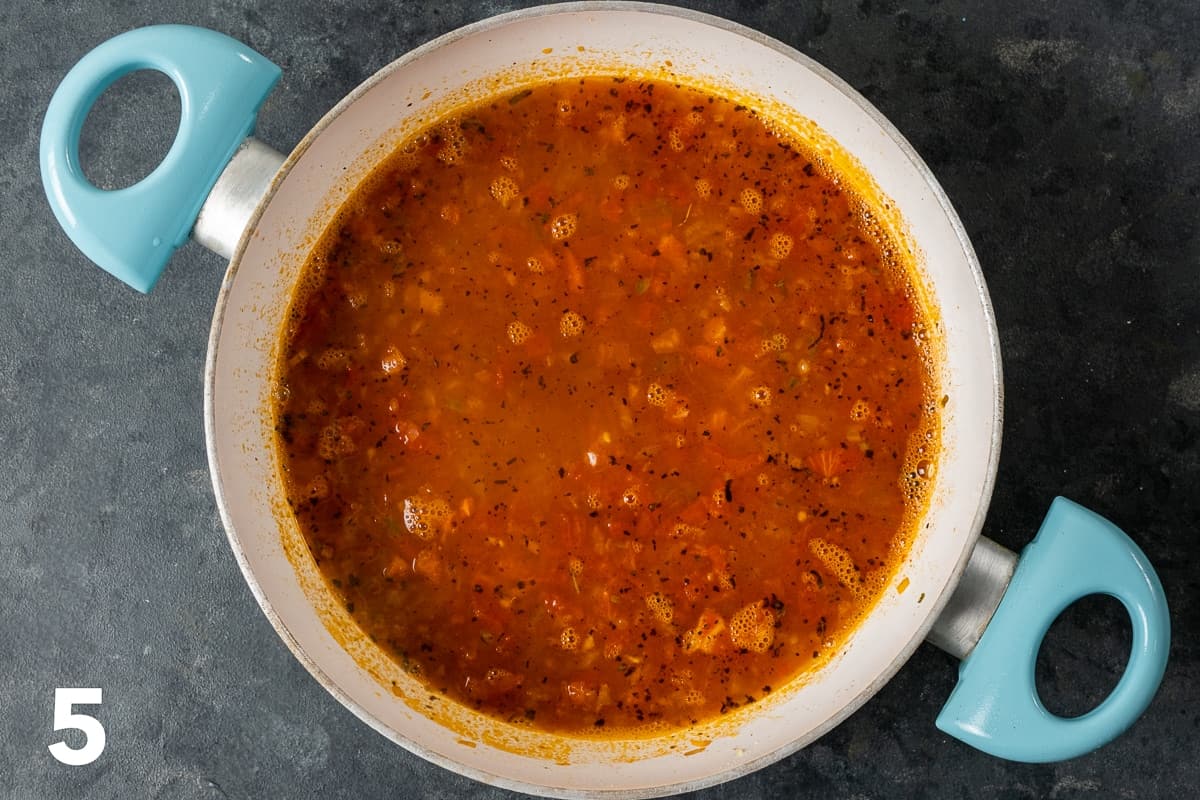 Bulgur and spicy tomato and onion mixture with hot water in a white pan.