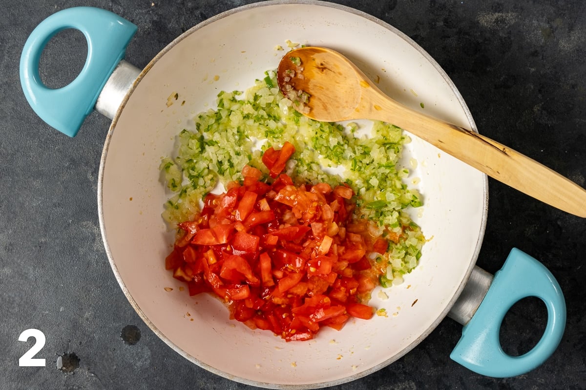 Finely chopped tomatoes, onions and peppers in a white pan and a wooden spoon inside it.