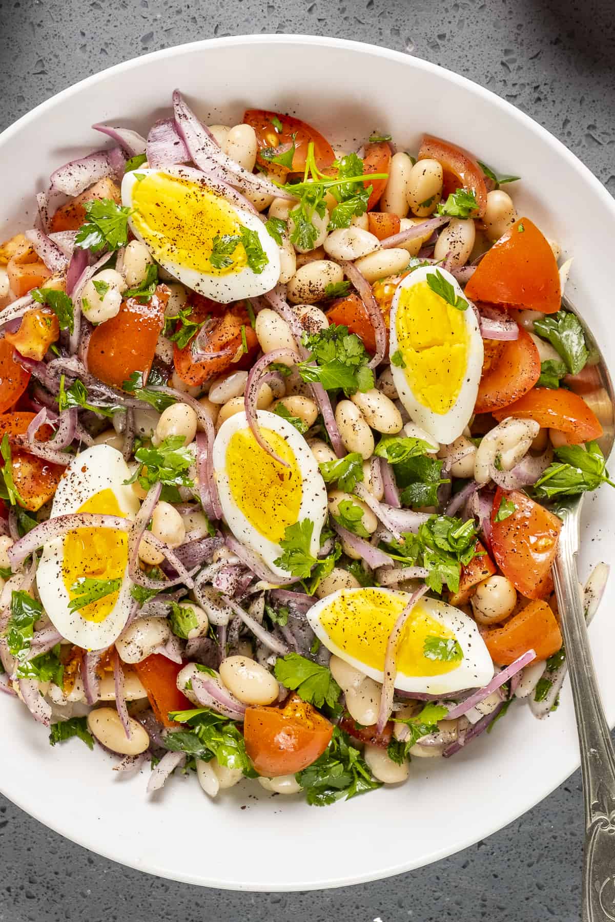 Bean salad with tomatoes and eggs in a white bowl.