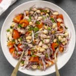 White bean salad with tomatoes and red onions in a white bowl.