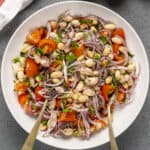 White bean salad with tomatoes and red onions in a white bowl.