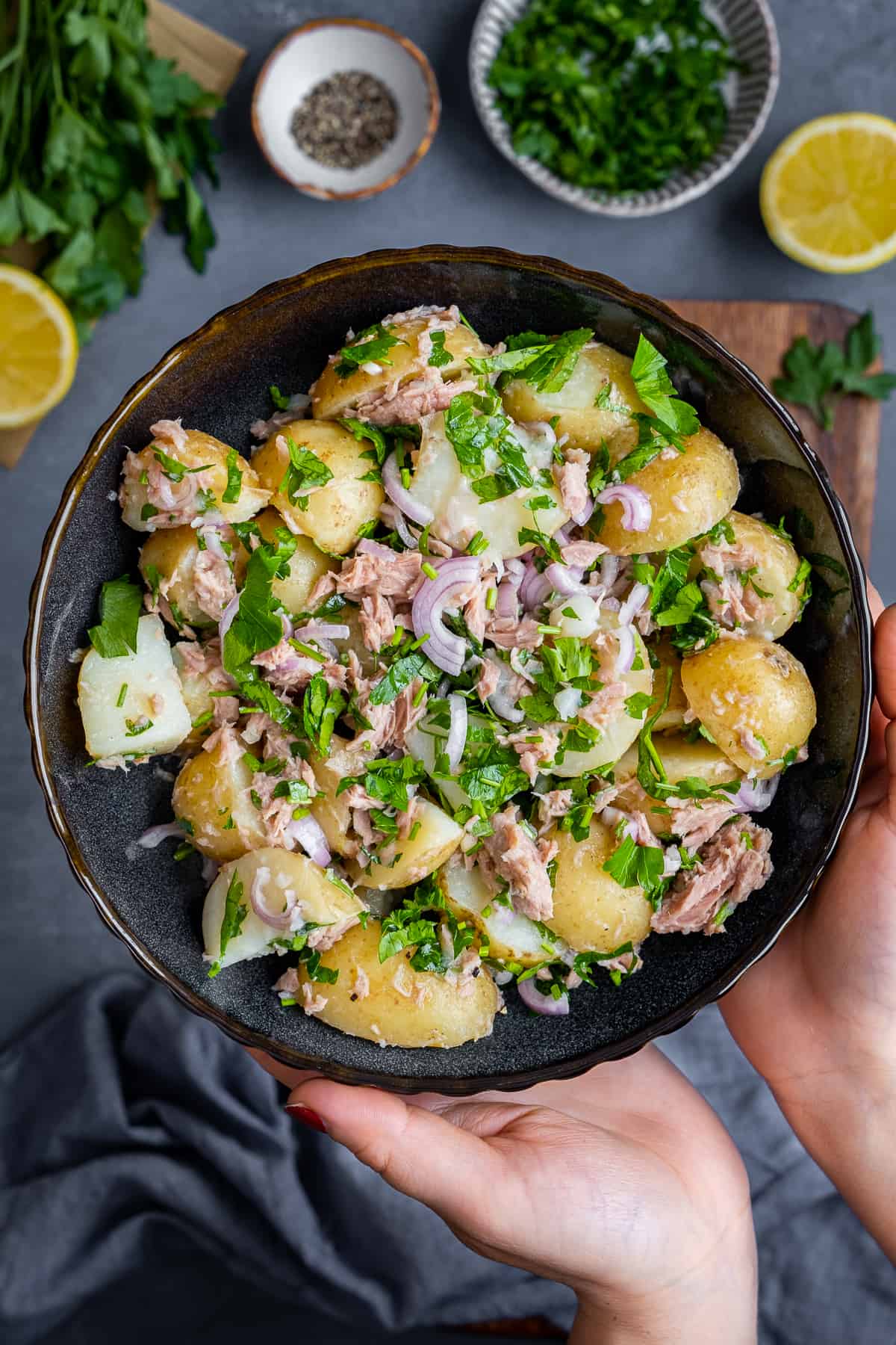 Hands holding a bowl of tuna potato salad photographed from top view.