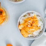 Rice porridge recipe topped with cinnamon, orange jam, kumquats and almonds served in white ceramic bowls.