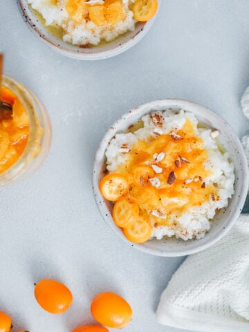 Rice porridge recipe topped with cinnamon, orange jam, kumquats and almonds served in white ceramic bowls.