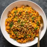 Spicy tomato bulgur pilaf topped with green lentils and parsley in a white bowl with a spoon inside it.