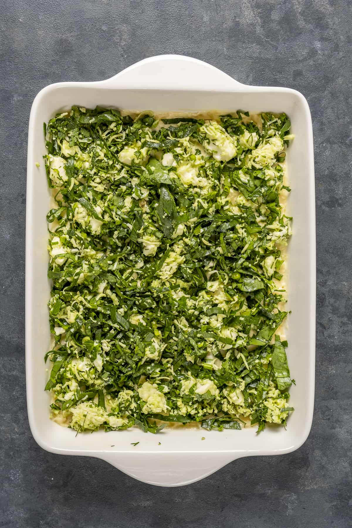 Spinach and cheese mixture spread on a stack of phyllo sheets in a baking pan.