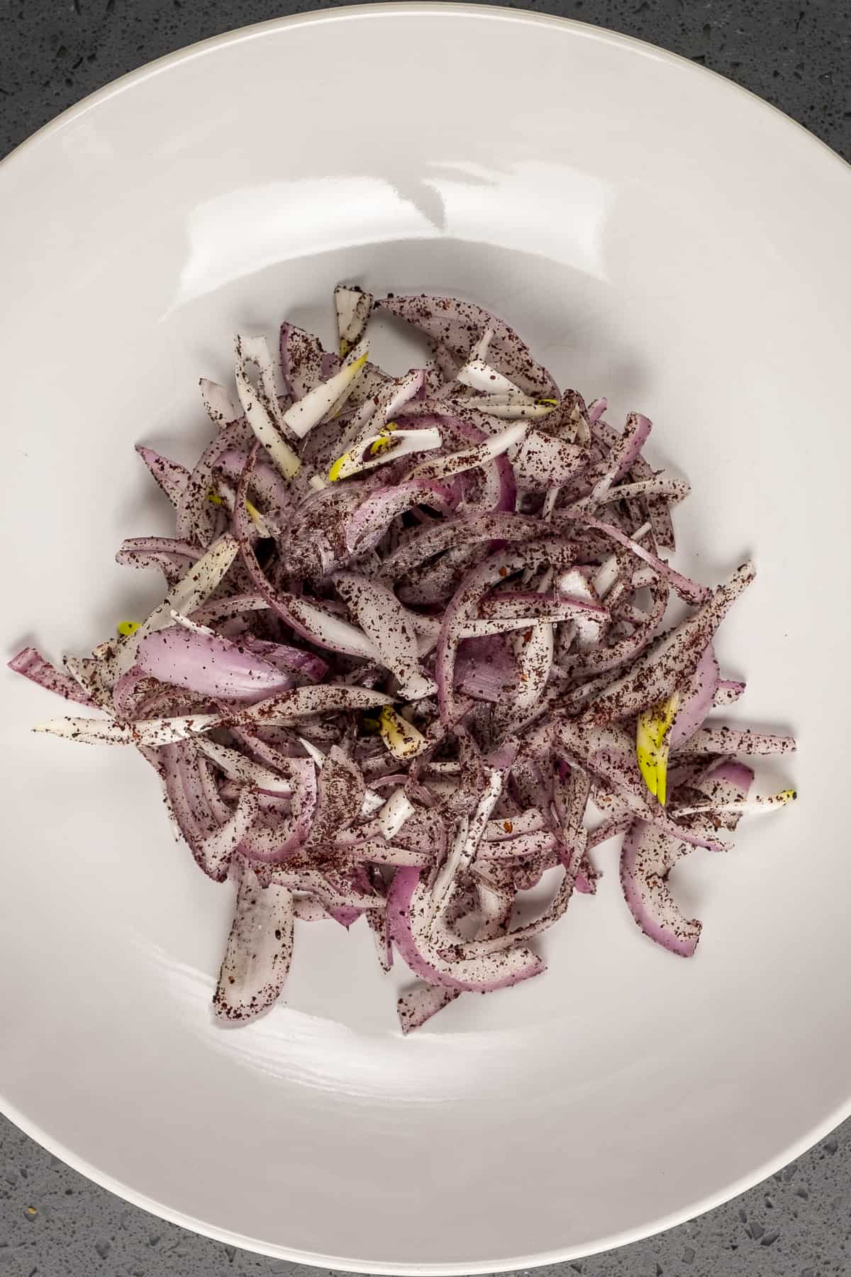 Red onions with sumac in a white bowl.