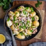 Tuna potato salad served in a black bowl and a fork inside, lemon halves, parsley and black pepper on the side.
